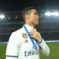 a soccer player is holding his medal in front of the crowd at a stadium as he looks off into the distance