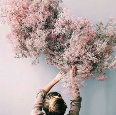 a woman is reaching up to pick flowers from the top of a tree with her hands