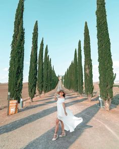 a woman in a white dress is walking down the road with trees on both sides