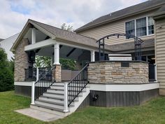 a house with stone and metal railings on the front porch, next to a covered patio