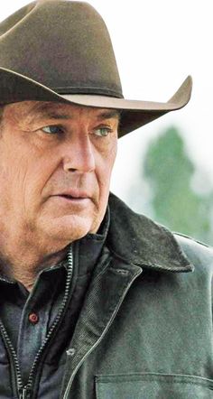 an older man wearing a leather jacket and hat looking off to the side with trees in the background