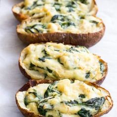 three pieces of bread with cheese and spinach on them sitting on a white surface