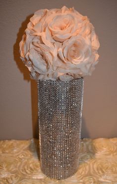 a silver vase with white flowers in it on a tableclothed surface, next to a wall