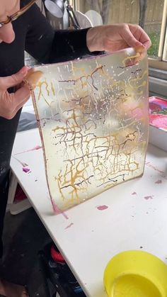 a woman is working on a piece of art with gold paint and acrylic