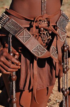 a woman wearing a brown belt with beads and chains around her waist is standing in the desert