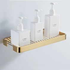 three soap dispensers are sitting on a gold shelf in front of a white wall