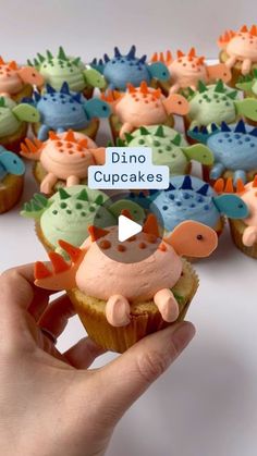 a person holding up a cupcake with dinosaur decorations on it's top and the words dino cupcakes above them