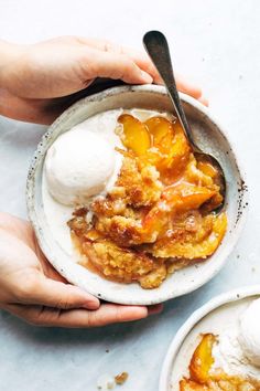 two hands holding bowls of food with ice cream on top and one bowl filled with peach cobbler