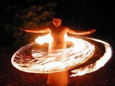 a woman is spinning fire around in the dark with her arms outstretched and hands out