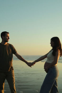 a man and woman holding hands on the beach