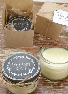 two candles in small boxes next to each other on a wooden table with tags and twine