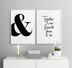 two black and white art prints on the wall above a dresser with a candle, books, and plant