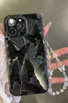 a person holding up a cell phone case with butterfly design on the back and chain attached to it