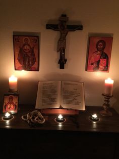 three candles are lit in front of an open book with pictures on the wall behind it