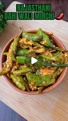 a bowl filled with cooked green peppers on top of a wooden table next to a plant