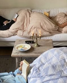 two people laying on a couch with candles in front of them and an open book