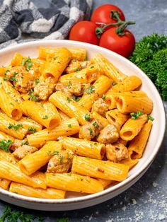 a bowl full of pasta with meat and parsley on the side next to tomatoes