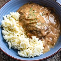 a blue bowl filled with rice and meat covered in gravy on top of a wooden table