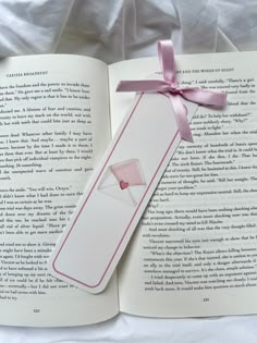 an open book with a pink ribbon tied around it and a white envelope in the middle