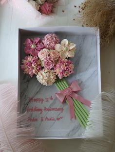 a bouquet of flowers in a box with pink ribbon on the inside and white feathers around it