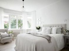 a bedroom with white walls and wooden flooring has a large bed, two chairs, and a window