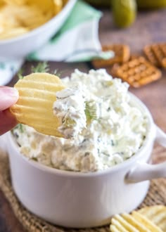 a hand holding a cracker over a bowl of dip with chips on the side