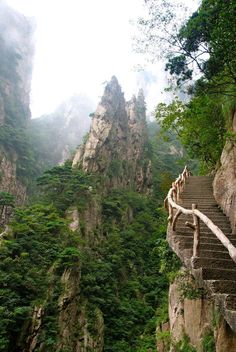 stairs leading up to the top of a mountain with trees on both sides and mountains in the background