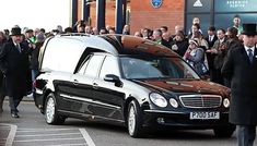 a man in a suit and tie walking next to a black car