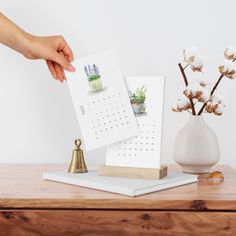 a desk with two calendars and a bell on it, next to a small potted plant