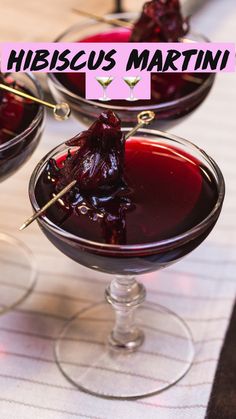 three glasses filled with red liquid sitting on top of a white tablecloth covered table