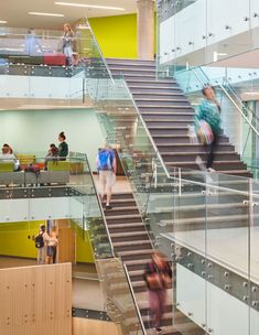 people walking up and down the stairs in an office building with glass balconies