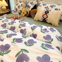 a bed with purple flowers and green leaves on it, next to a night stand