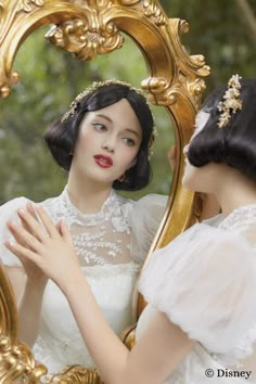 a woman is looking at herself in the mirror while wearing a white dress and gold jewelry