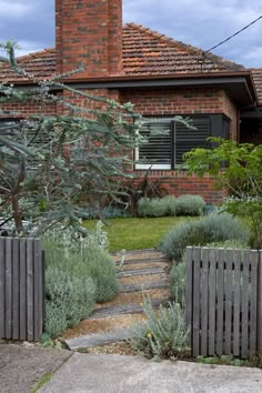 a brick house with a wooden fence in front of it and bushes growing on the side