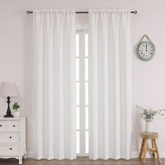 a room with white curtains and a clock on the wall next to a dresser in front of it