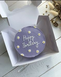 a purple birthday cake with daisies in a white gift box on a wooden table