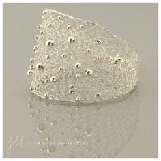 a white lace bracelet with silver beads on the top and bottom, sitting on a reflective surface