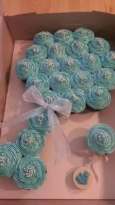 cupcakes in a box with ribbon and bow on the top one is made out of blue icing