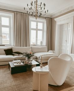 a living room filled with furniture and a chandelier hanging from the ceiling in front of two windows