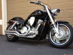 a black motorcycle parked in front of a garage door next to a driveway with no cars on it