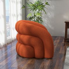 an orange chair sitting on top of a hard wood floor next to a potted plant