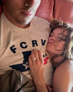 a woman laying next to a man on top of a red couch with her arm around him