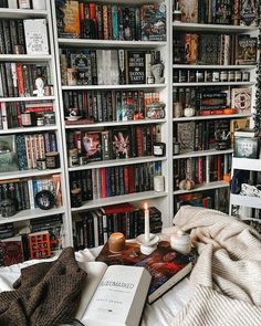 a book shelf filled with lots of books next to a white bed covered in blankets