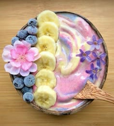 a bowl filled with fruit and flowers on top of a wooden table next to a spoon