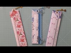 three paper bookmarks are hanging on the wall with string attached to them, one is pink and one is blue