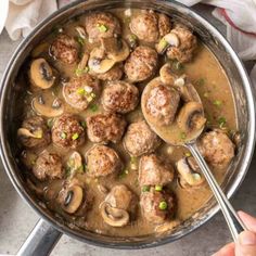 a pan filled with meatballs and mushrooms on top of a table next to a spoon