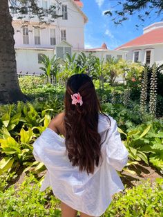 a woman with long brown hair wearing a white shirt and pink flower in her hair