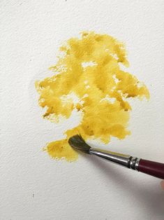 a person holding a paintbrush and painting yellow on white paper with watercolors