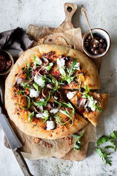 a pizza sitting on top of a wooden cutting board next to a bowl of olives