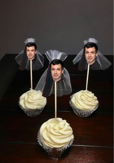 three cupcakes with white frosting on top of them and two men's heads behind them